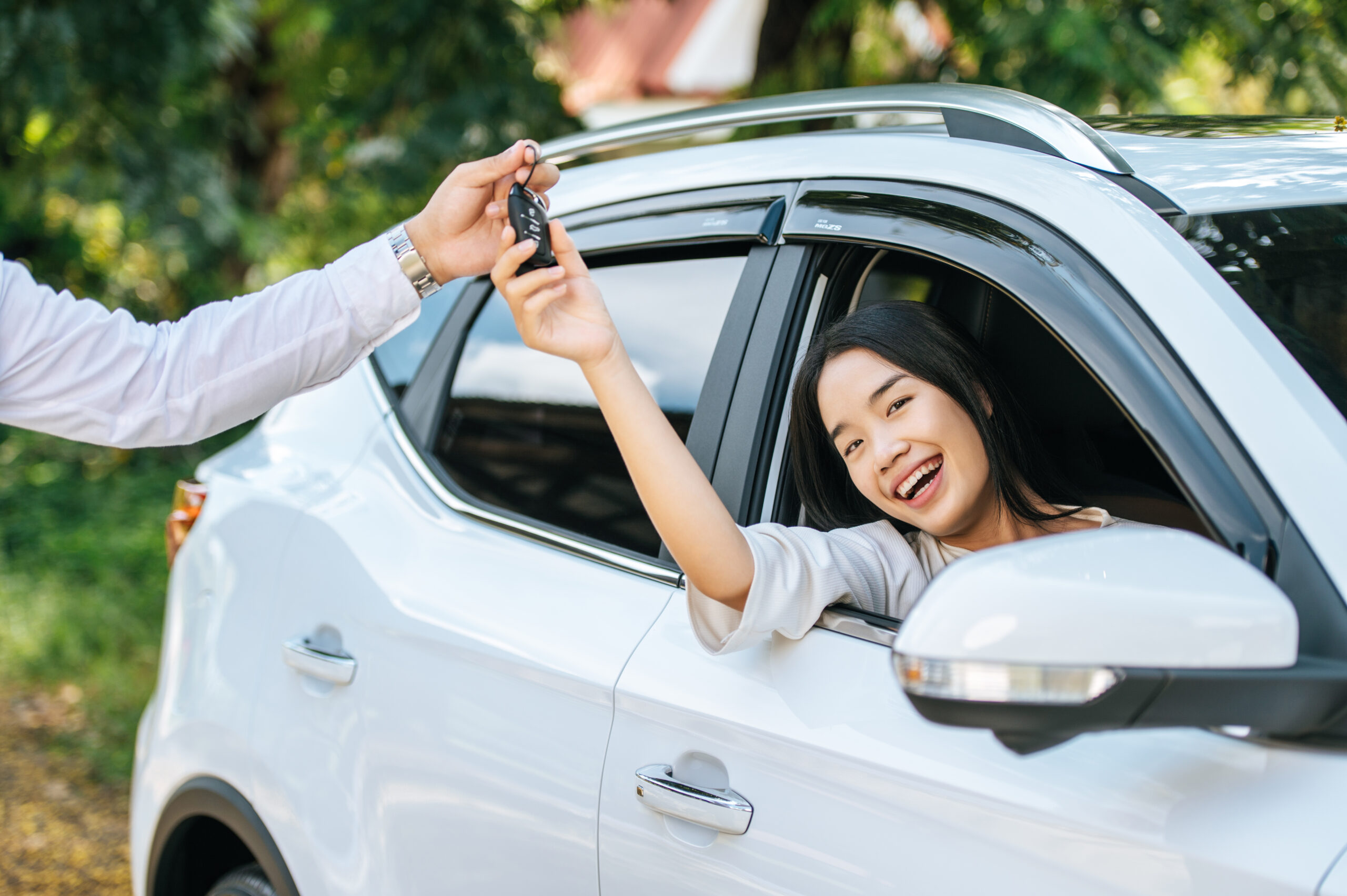 Happy customer receiving car keys while sitting in a white SUV, symbolizing new car ownership and the importance of car insurance